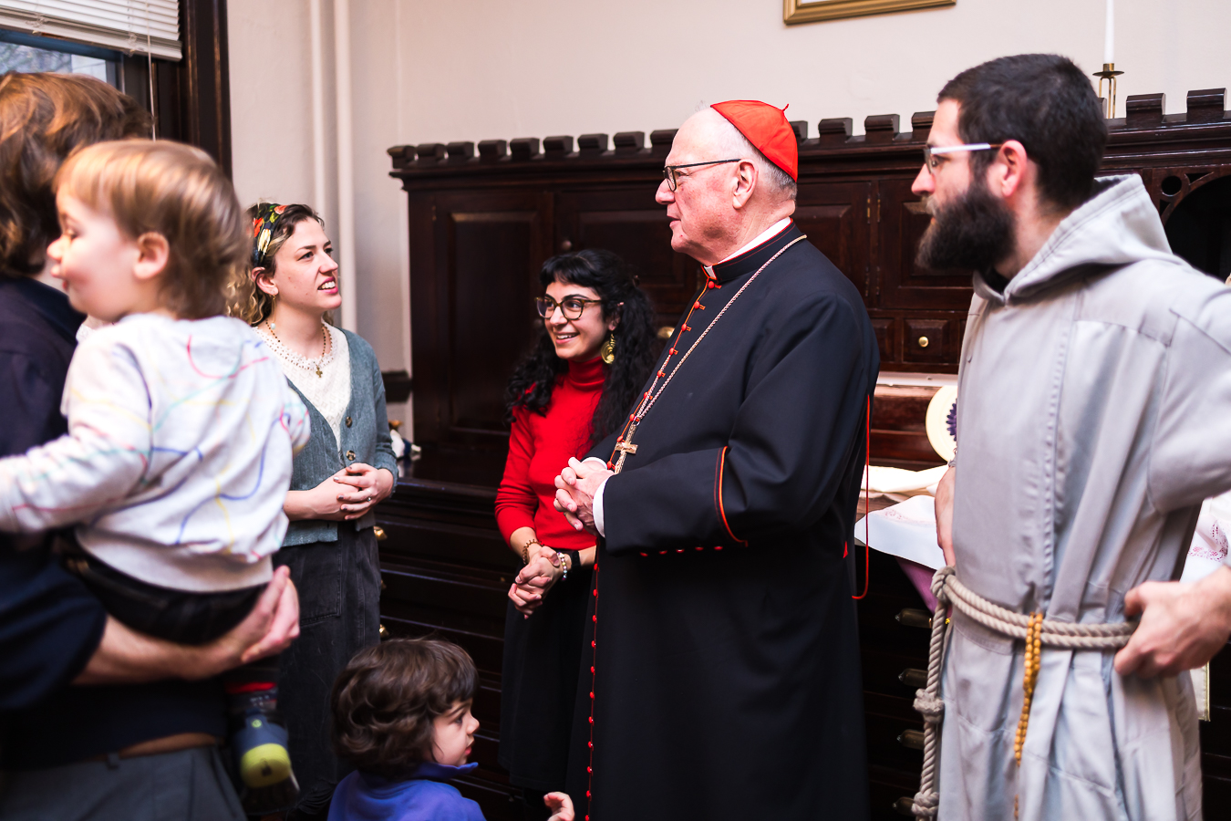 Erin McAtee (left, wearing the colorful headband) and Claire Majewski (right, in the red sweater) chat with Cardinal Timothy Dolan before one of Arthouse 2B's masses for artists in March 2024. (Photo by Edwin Lucero)