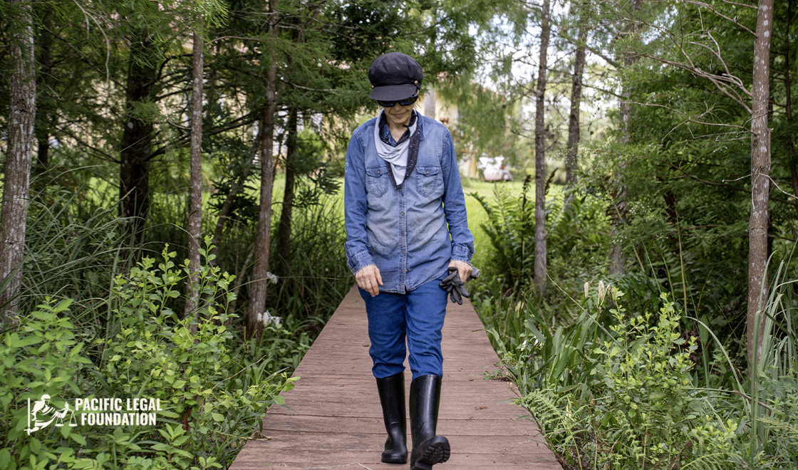 A woman wearing a hat and boots walking on a wooden path