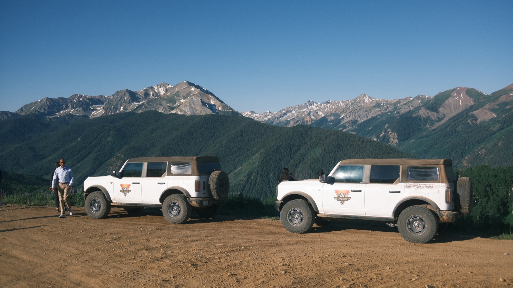 Two cars parked on a dirt road with mountains in the background