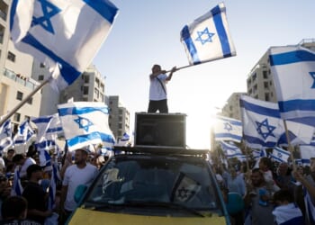 A man standing on top of a car with a flag on top