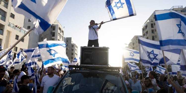A man standing on top of a car with a flag on top