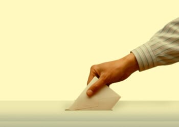 A hand putting a piece of paper into a ballot box