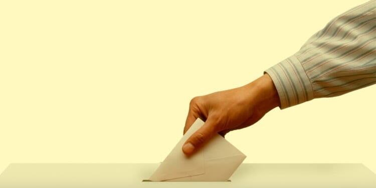 A hand putting a piece of paper into a ballot box