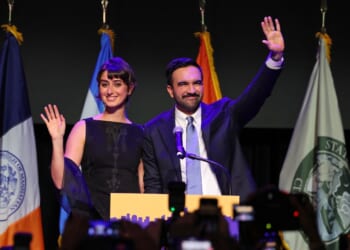 A man and woman standing on a stage with a microphone and a flag behind them