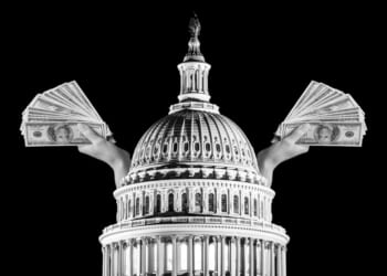 A hand holding money in front of a dome with United States Capitol in the background