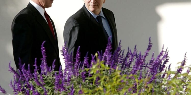 A pair of men in suits standing next to purple flowers