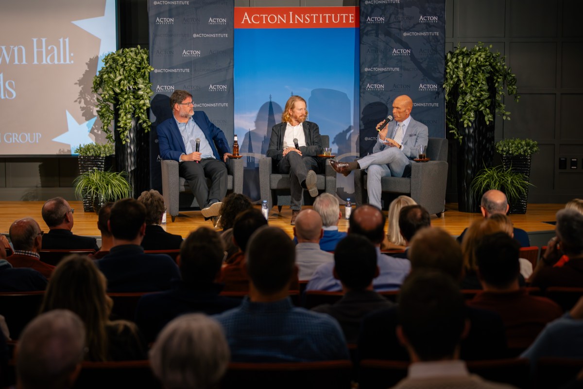 A group of men sitting in chairs on a stage with a crowd of people