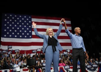 A man and woman holding hands up in front of a flag