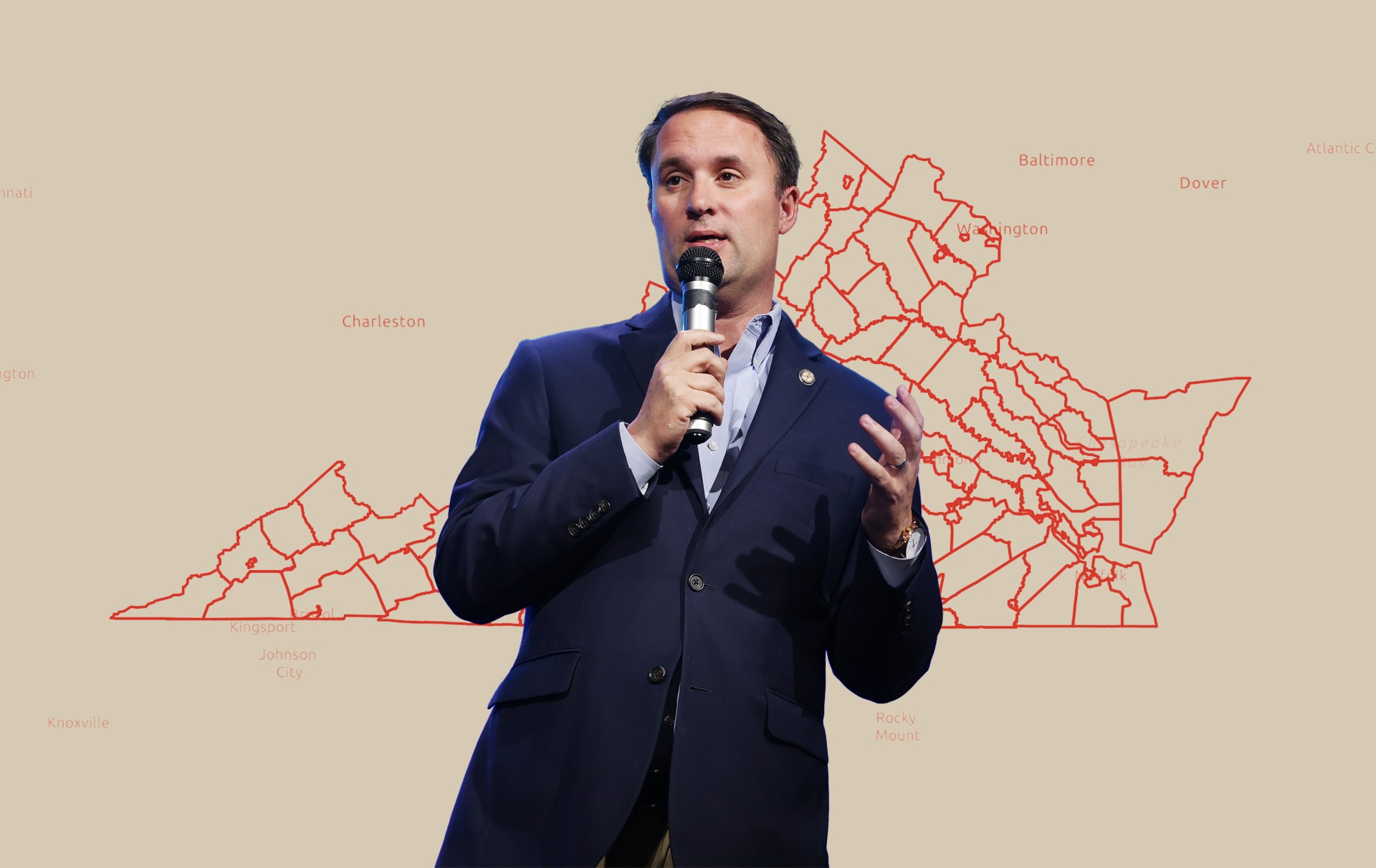 A man in a dark blue blazer speaks into a microphone while standing in front of a beige background displaying a red outline map of Tennessee with labeled cities.