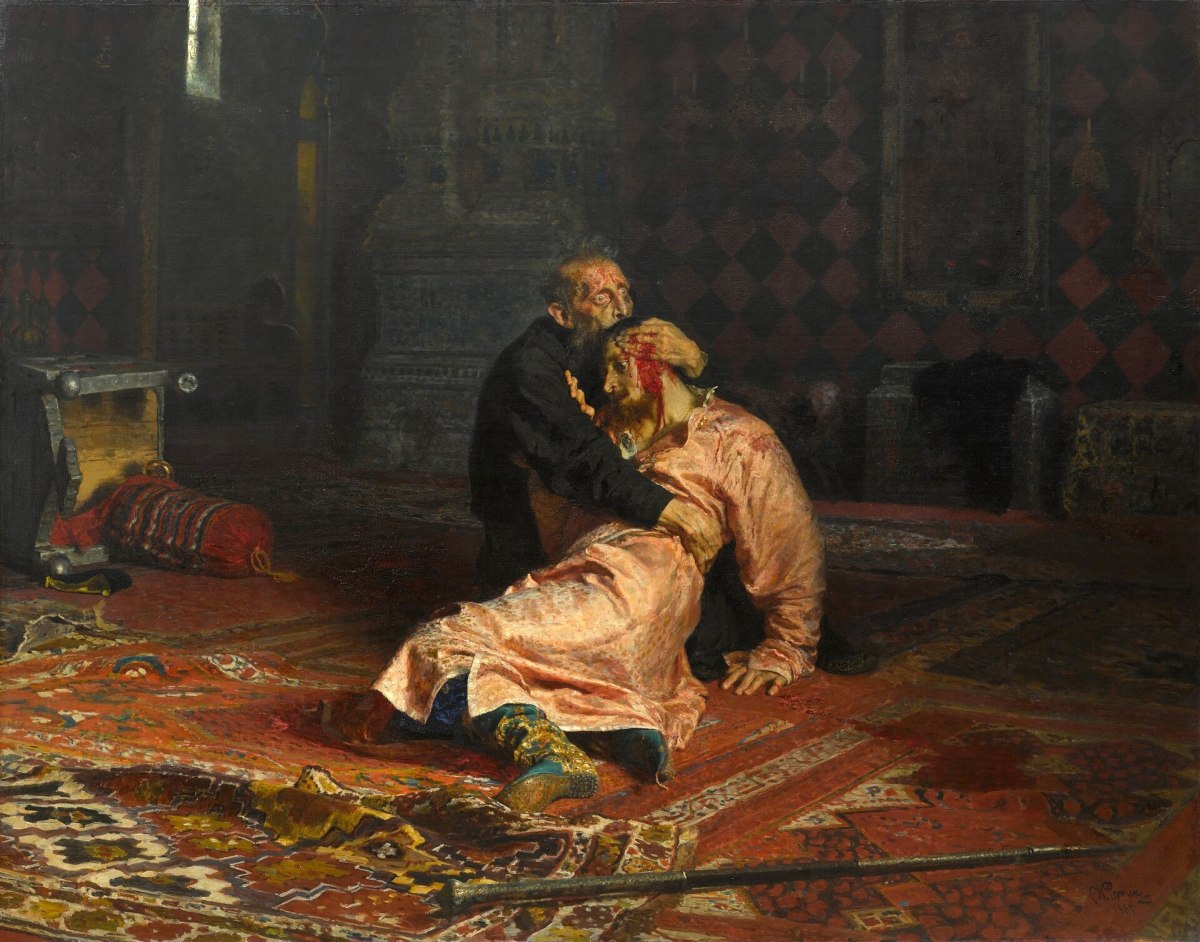 # Alt Text An elderly bearded man in dark robes kneels on an ornate red carpet beside a prone figure in a golden robe within a dimly lit interior, suggesting a dramatic historical or religious scene.