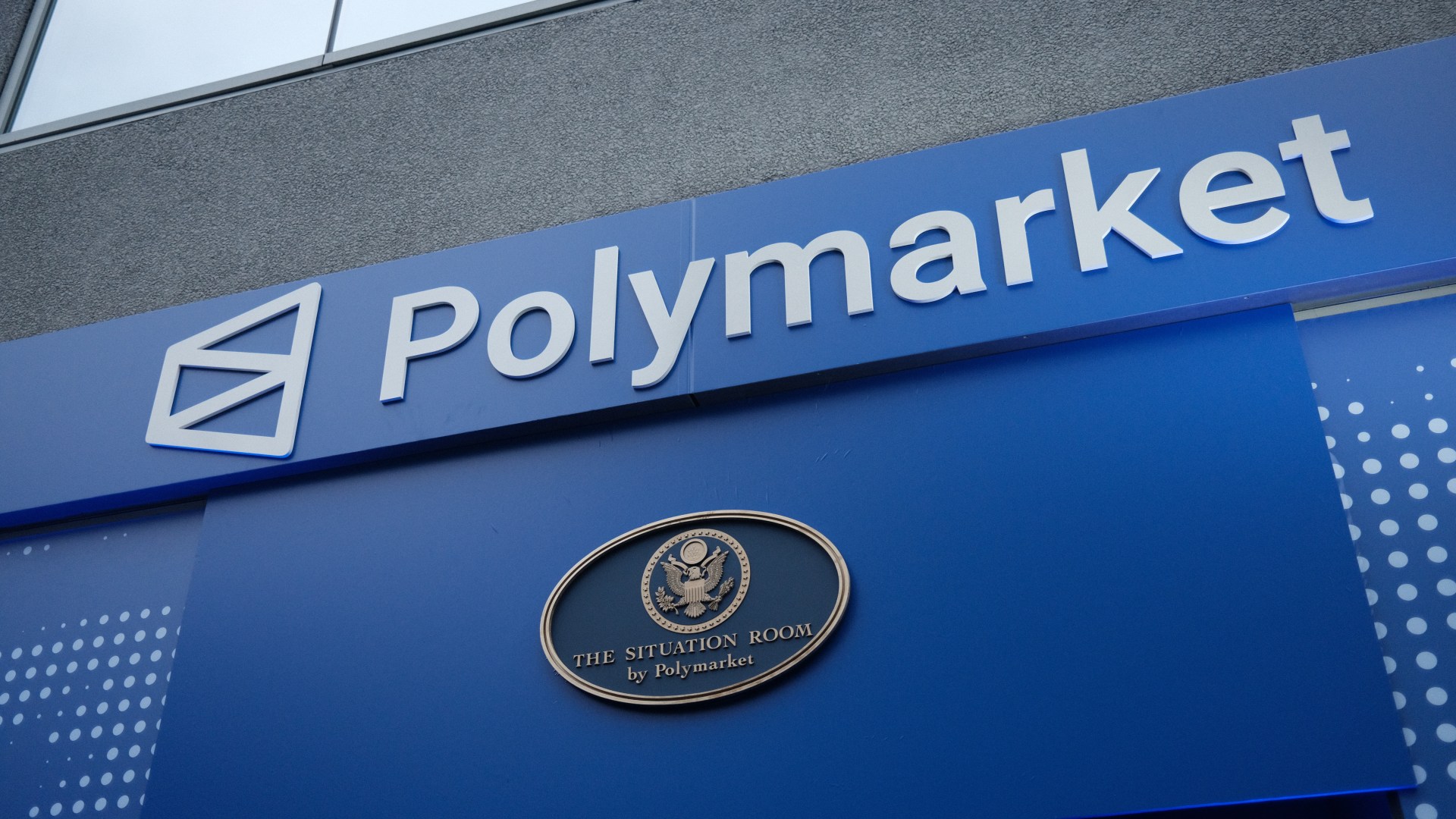 A blue Polymarket storefront signage with a logo and an oval plaque reading "The Situation Room by Polymarket" featuring the U.S. Great Seal.