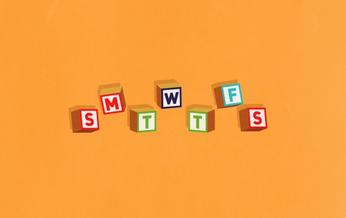Colorful wooden blocks spelling "SMWTTFS" arranged in a row against an orange background.