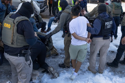 # Alt Text Law enforcement officers, including ICE and ERO agents, detain a person during an operation in a snowy outdoor setting.