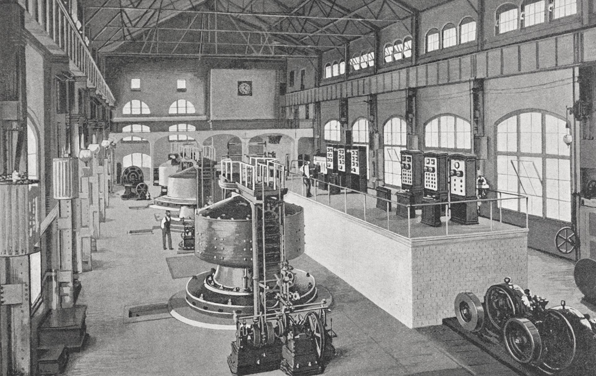 A historical black and white photograph of an industrial power plant interior featuring large turbine generators, control panels, workers, and expansive windows throughout the multi-level factory building.