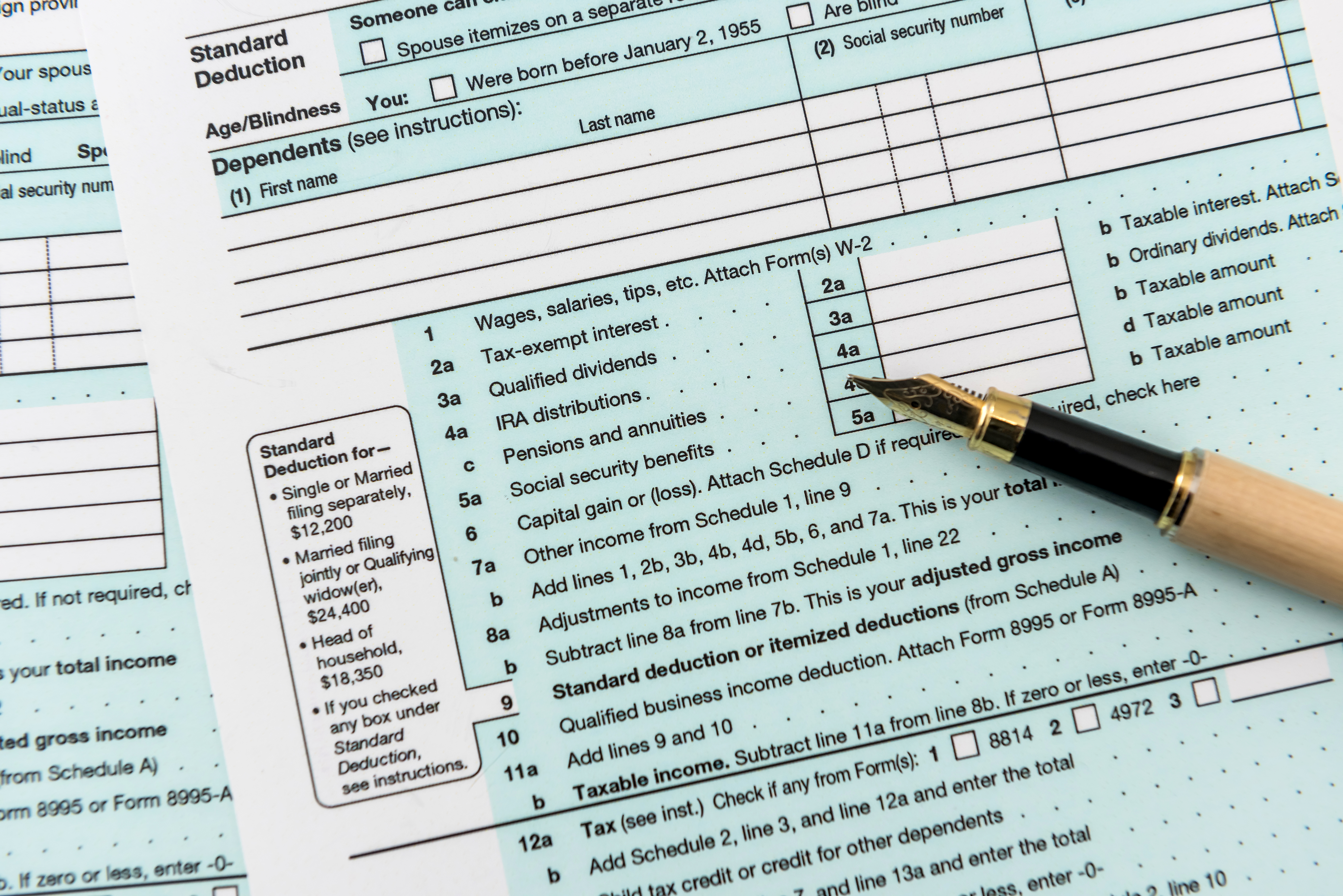 A fountain pen rests on a U.S. Form 1040 tax return document, displaying various income sections and standard deduction information.